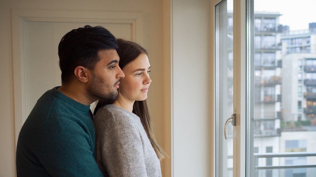 Bilde av mann og kvinne som står sammen og ser ut av et vindu. Foto.