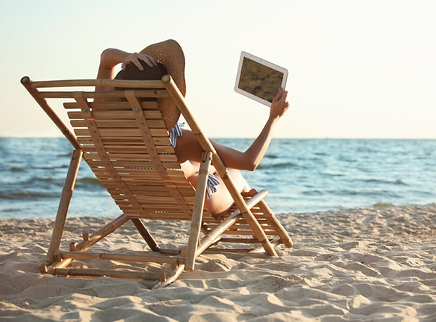 Person som sitter i solstol på stranden. Foto.
