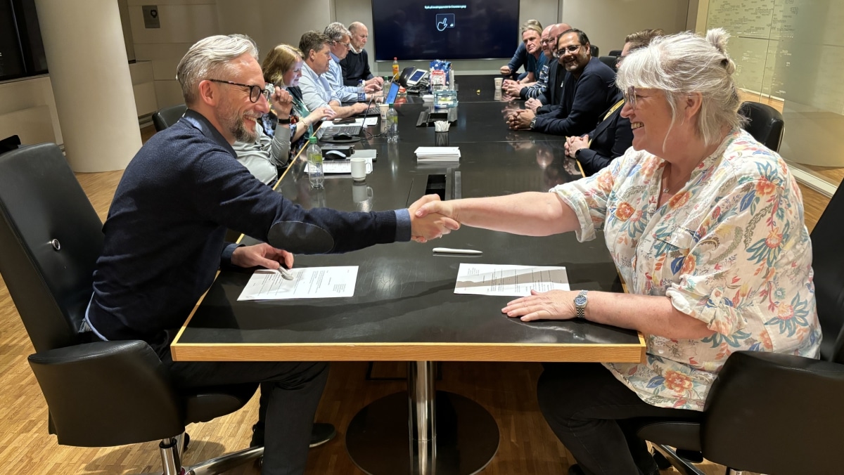 Personer som håndhilser rundt konferansebord. Foto.